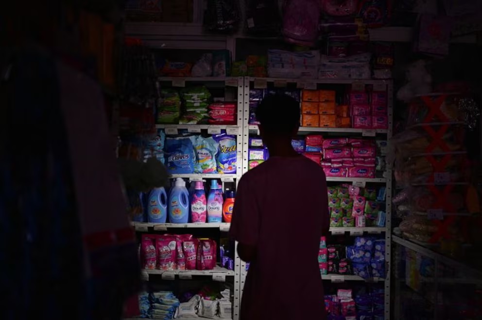Por un apagón en Caracas, un hombre ilumina con su celular para encontrar mercadería en un negocio.